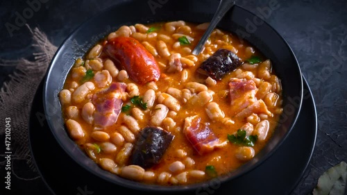 Traditional recipe of beans with chorizo and blood sausage called “Fabada Asturiana” on a dark table with some ingredients around. Typical Spanish food with “compango”.  photo