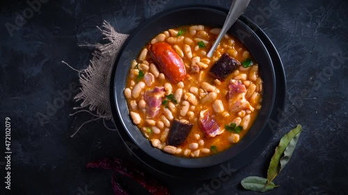 Traditional recipe of beans with chorizo and blood sausage called “Fabada Asturiana” on a dark table with some ingredients around. Typical Spanish food with “compango”.  photo