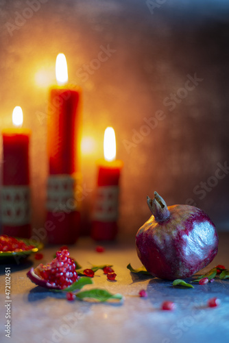 Ripe juicy pomegranate on the background of burning red candles.