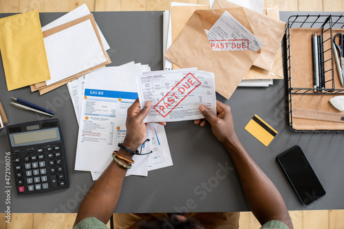 High angle view of unrecognizable blackman sitting at table with bills and checking arrears of payment