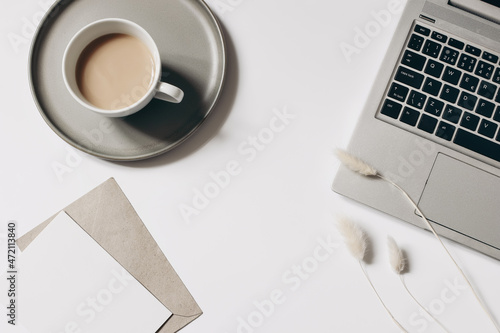 Elegant workspace composition. Cup of coffee, dry lagurus grass and laptop isolated on white table background. Blank greeting card mockup with envelope. Flat lay, top view. Blogger, home office.
