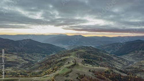 Bird's-eye timelapse of the road passing through the autumn forest in the mountains under a cloudy sky