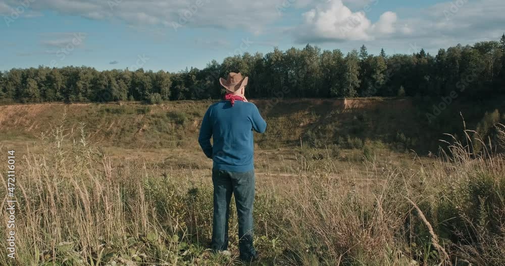 Man in a cowboy hat stands on the edge of a sandy ravine overgrown with forest and smokes a cigarette. There is wild nature around, it is evening Man in a cowboy hat stands on the edge of a sandy ravine overgrown with forest and smokes a cigarette. There is wild nature around, it is evening