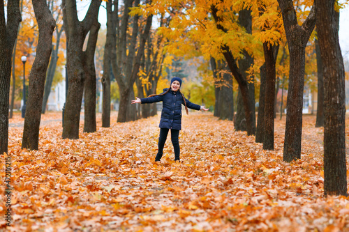 Portrait of a child girl walking in autumn city park. Beautiful nature, trees with yellow leaves.