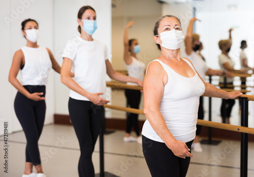 Dancing European woman in a protective mask  engaged in ballet in the studio during the pandemic  stand holding a barre 