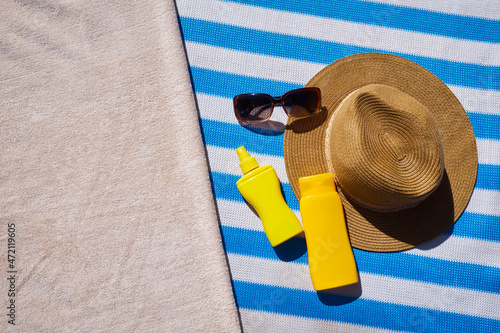 Yellow sunscreen cream bottles for skin protection, sun glasses, straw hat and beach towel on the blue striped mattress. Summer recreation concept. Flat lay