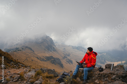  man sitting on the cliff edge with scenic view at the mountain. Distant work and travel, freelance as lifestyle concept
