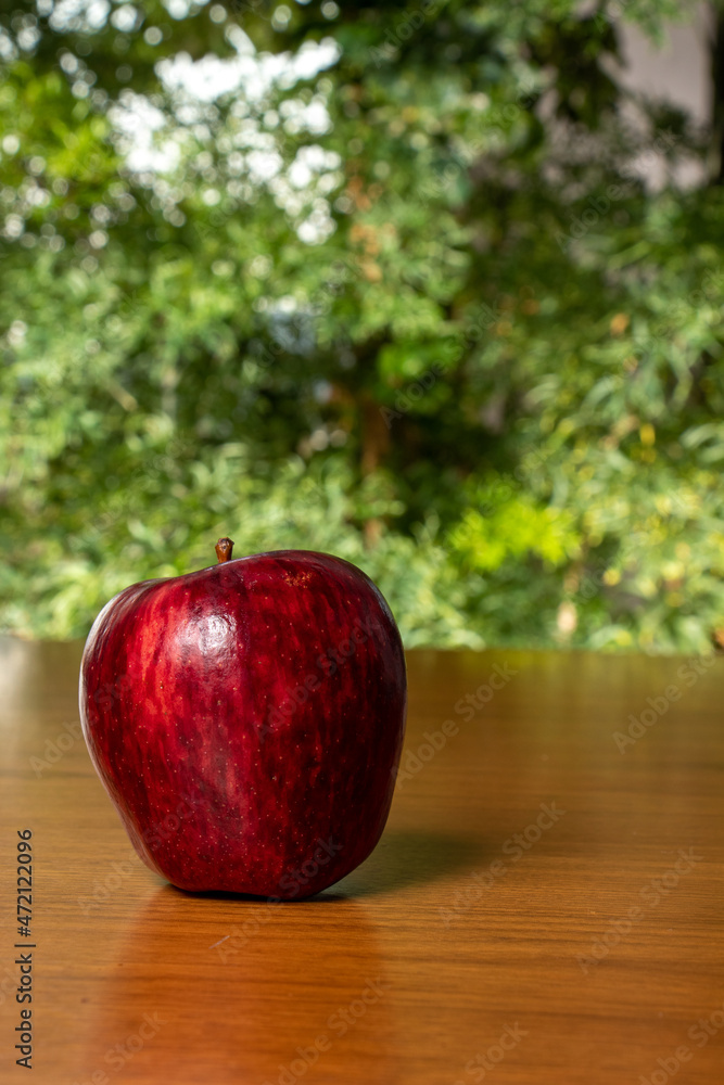 delicious red apple on wooden table, blurred green vegetation in the background, close up photo space for text delicious red apple on wooden table, blurred green vegetation in the background, close up photo space for text