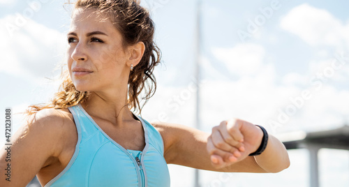 A smart watch for heart rate counting. A sporty lifestyle, the coach takes a break. Confident woman running city embankment, athletic figure, comfortable fitness clothes.