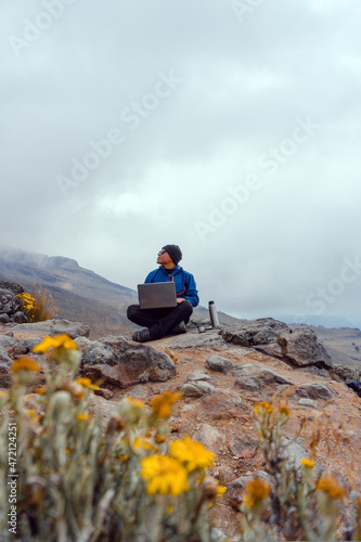 Young man drinking coffee in mountains with laptop. Mountain camping concept.