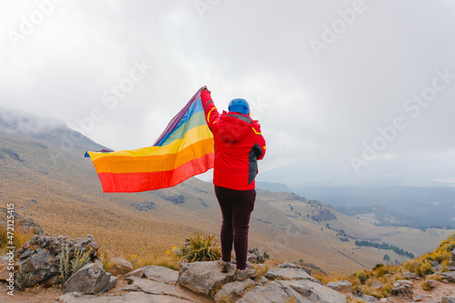 Woman holding the Gay Rainbow Flag on a mountain outdoors. Happiness, freedom and love concept for same sex couples