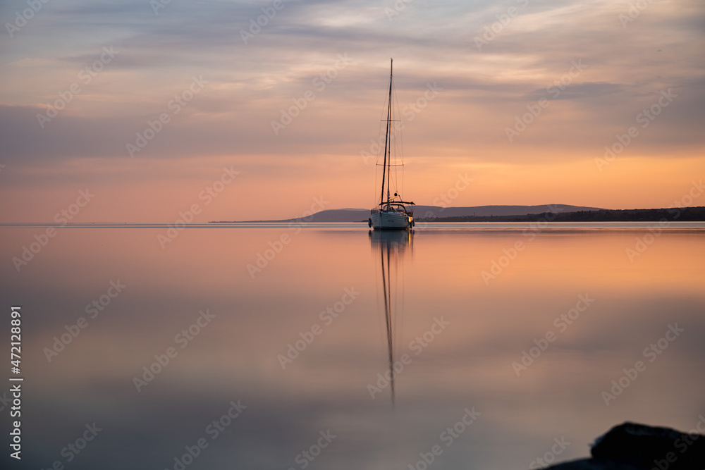 a sailing boat at sunset on a calm lake a sailing boat at sunset on a calm lake