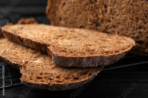 Cooling rack with slices of tasty rye sodawater bread on black wooden table, closeup photo