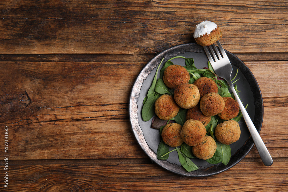 Delicious falafel balls with spinach and sauce on wooden table, top view. Space for text Delicious falafel balls with spinach and sauce on wooden table, top view. Space for text