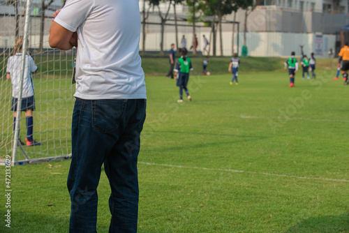 Father standing and watching his daughter playing football in a school tournament on a sideline with a sunny day. Sport, outdoor active, lifestyle, happy family and soccer mom and soccer dad concepts. © athichoke.pim