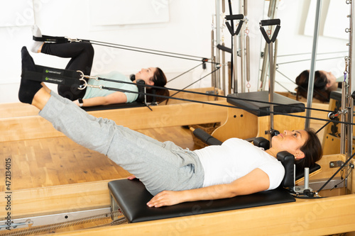 Side view of focused sportswoman stretching body on pilates chair while doing forward bends during workout