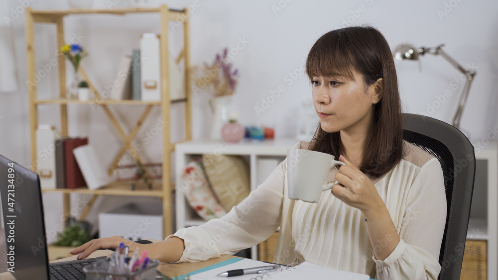 gorgeous asian korean female entrepreneur with cup of coffee in hand is replying an important email on notebook