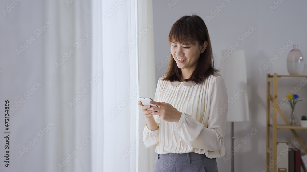 beautiful asian female manager taking break from work and browsing funny posts on social media with her smartphone.