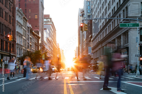 Busy street scene is crowded with people at an intersection on Fifth Avenue in New York City with sunlight shining between the buildings © deberarr
