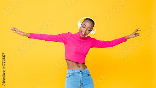 Portrait of happy African American woman wearing headphones listening to music and dancing on colorful yellow isolated background