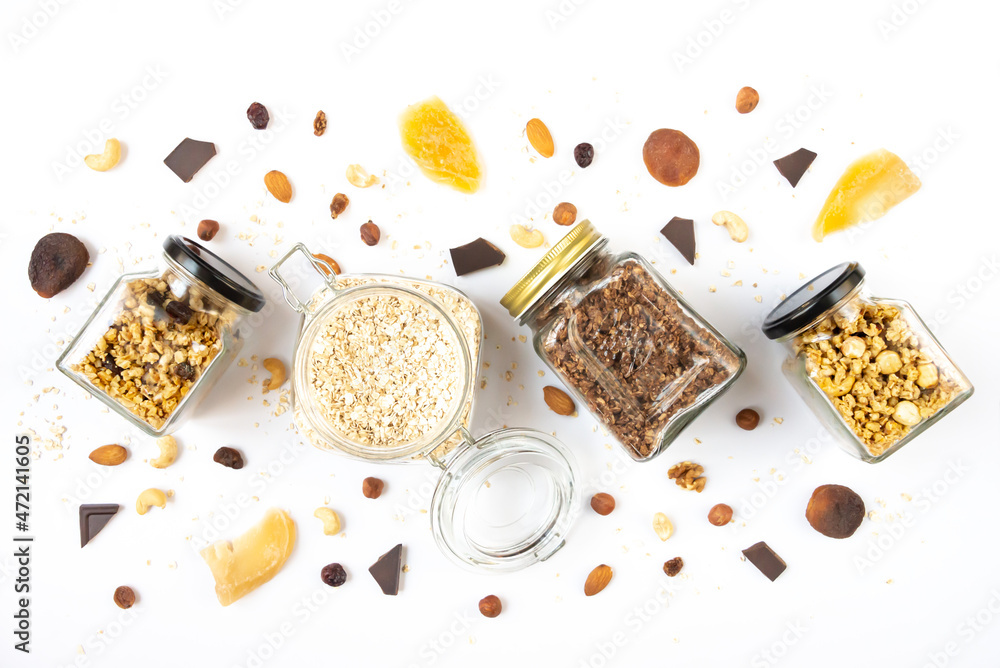 Top view of jars full of oats and various crunchy granola with ingredients scattered around - dried fruits, nuts and chocolate bars. Healthy eating concept.