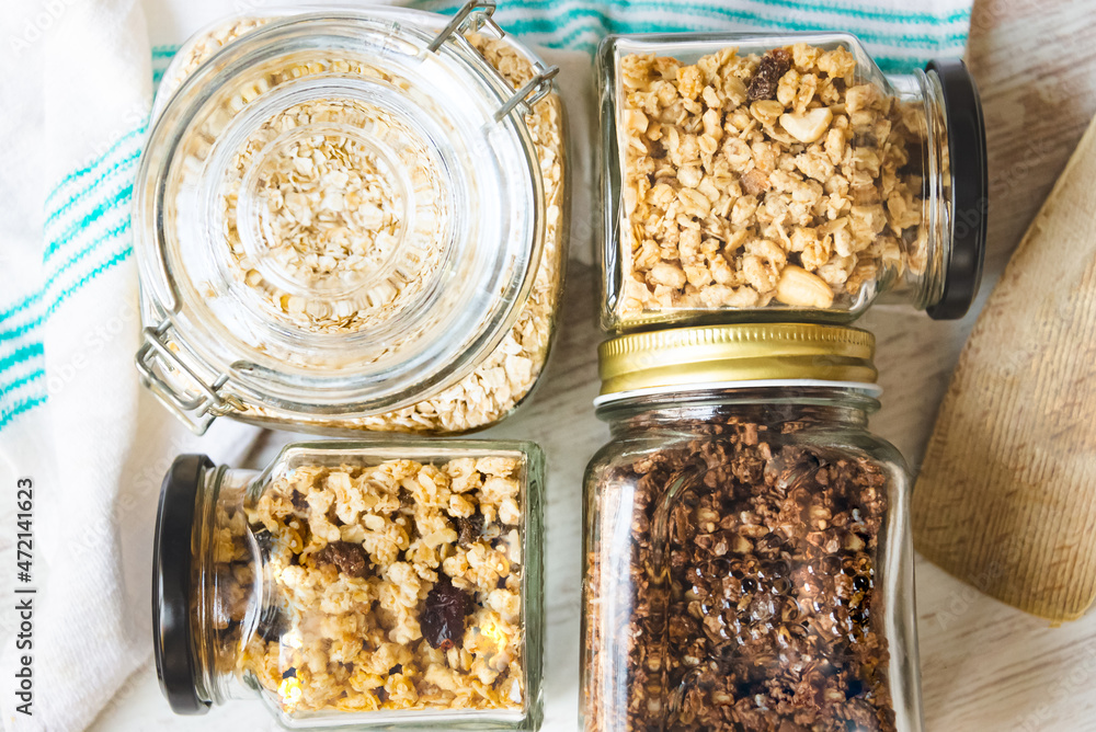 Top view of jars full of oats and various crunchy granola - plain, dried fruits, nuts and chocolate. Healthy eating concept.