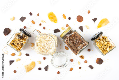Top view of jars full of oats and various crunchy granola with ingredients scattered around - dried fruits, nuts and chocolate bars. Healthy eating concept.