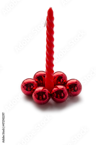 A thin twisted red candle with a white wick. There are six glossy red balls at the base. White background