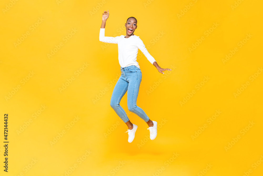 Energetic happy young African American woman jumping with hand up in isolated yellow studio background