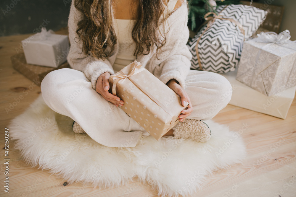 Young beautiful woman holding gift box in a cozy room with Christmas tree and presents on background. Young beautiful woman holding gift box in a cozy room with Christmas tree and presents on background.