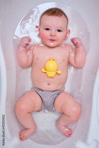 Infant baby plays with toys while lying in a children bath. A baby at the age of four months bathes in water