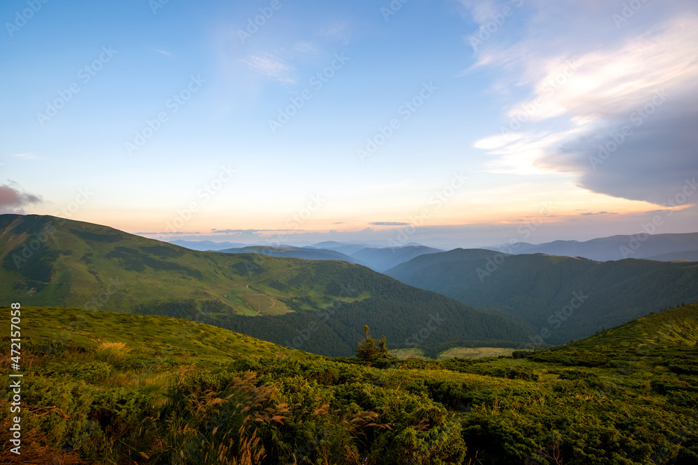 Summer evening mountain landscape with grassy hills and distant peaks at colorful sunset