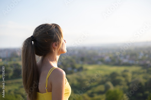 Fotografi Young relaxed woman standing in green field looking at sunset view in evening nature