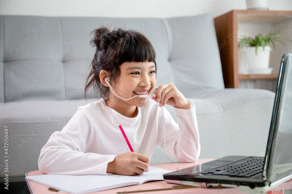 Asian girl students wear headphones study online with video call the teacher, Happy young girl learning earth ecology listen lecture watch write notes look at the laptop at home.Covid-19 coronavirus. Asian girl students wear headphones study online with video call the teacher, Happy young girl learning earth ecology listen lecture watch write notes look at the laptop at home.Covid-19 coronavirus.