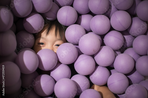 little child looking happy covered by purple balls in ball pit or pool photo