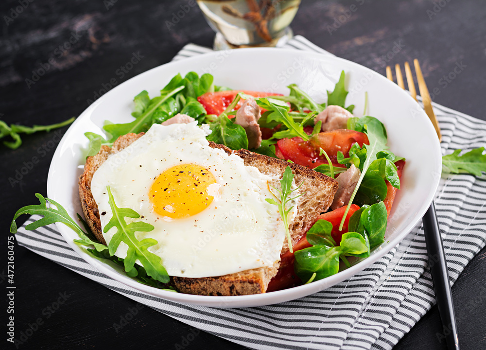 Breakfast - toast with fried eggs and tomatoes salad with greens and cod liver on dark background. Healthy breakfast. Breakfast - toast with fried eggs and tomatoes salad with greens and cod liver on dark background. Healthy breakfast.