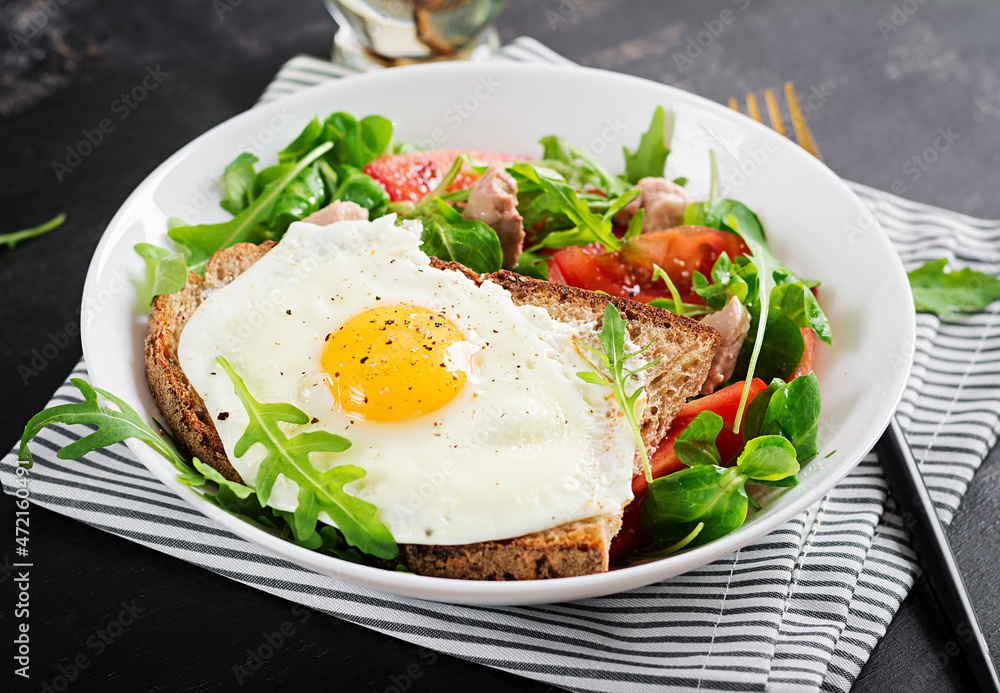 Breakfast - toast with fried eggs and tomatoes salad with greens and cod liver on dark background. Healthy breakfast. Breakfast - toast with fried eggs and tomatoes salad with greens and cod liver on dark background. Healthy breakfast.