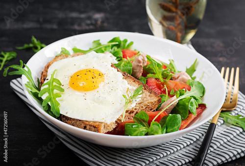 Breakfast - toast with fried eggs and tomatoes salad with greens and cod liver on dark background. Healthy breakfast.