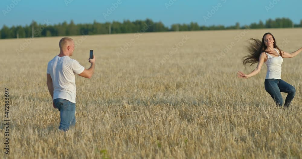 Male blogger shoots a video with a beautiful woman. Young woman is dancing in a field, she is posing for a videoshoot. Photo shoot in a wheat field. 4k, ProRes Male blogger shoots a video with a beautiful woman. Young woman is dancing in a field, she is posing for a videoshoot. Photo shoot in a wheat field. 4k, ProRes