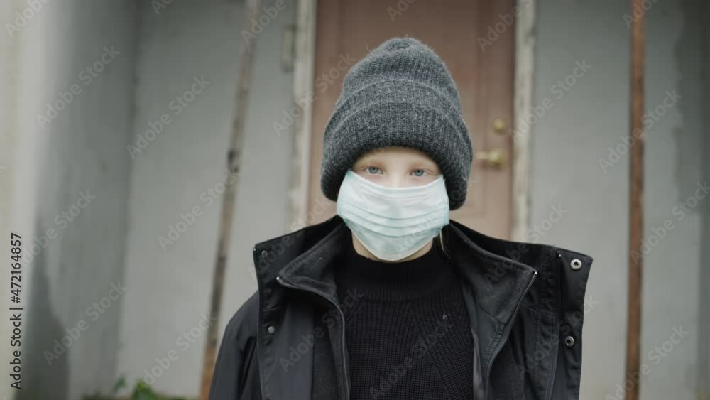Portrait of a child from a poor family. Standing on the threshold of his house in a protective mask Portrait of a child from a poor family. Standing on the threshold of his house in a protective mask