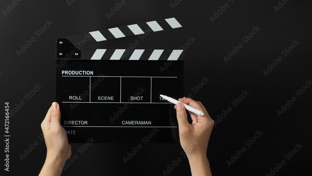 Hand is holding black clapper board or movie slate and marker Pen on black background