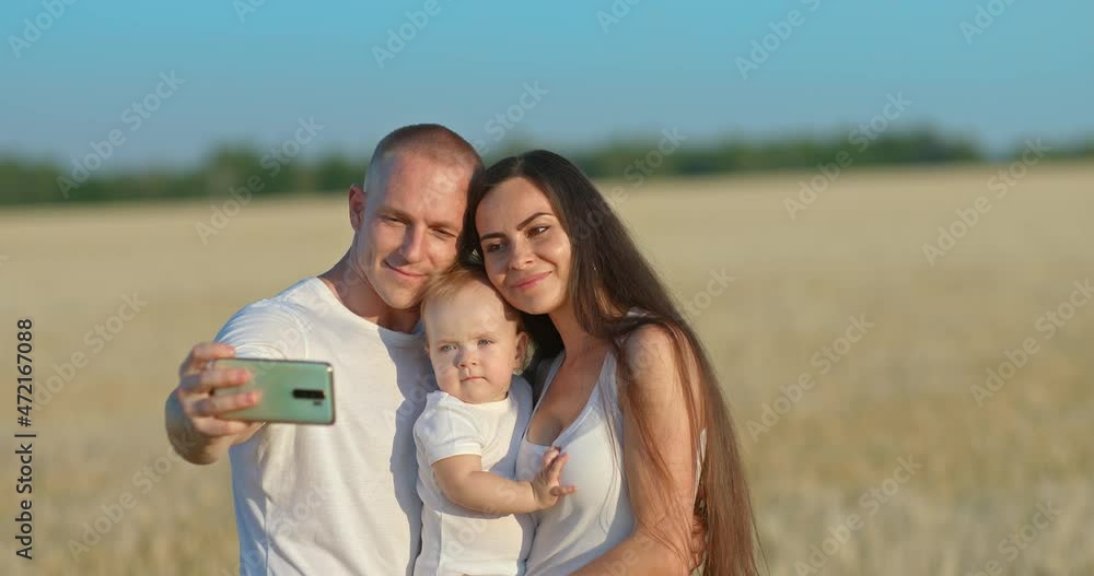 Family photo on a mobile phone. Young man takes a selfie with his wife and daughter on a mobile phone. Beautiful woman with a baby is smiling, a photo shoot in a wheat field. 4k, ProRes Family photo on a mobile phone. Young man takes a selfie with his wife and daughter on a mobile phone. Beautiful woman with a baby is smiling, a photo shoot in a wheat field. 4k, ProRes