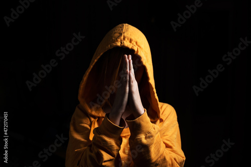 Unrecognizable woman with a hood put on her head praying on a black background. Front view.