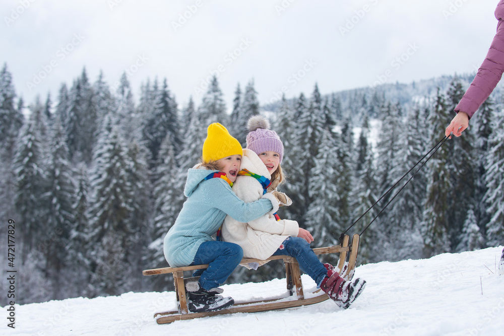 Children sledding, riding a sledge. Children son and daughter play in snow in winter. Outdoor kids fun for Christmas family vacation. Family christmas holiday outdoor.