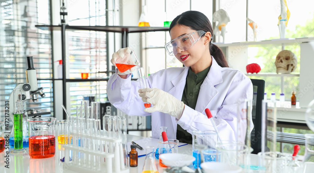 Asian woman as chemistry expert pouring experiment liquid from beaker into glass tube with safety protection of goggles and glove at scientific lab Asian woman as chemistry expert pouring experiment liquid from beaker into glass tube with safety protection of goggles and glove at scientific lab