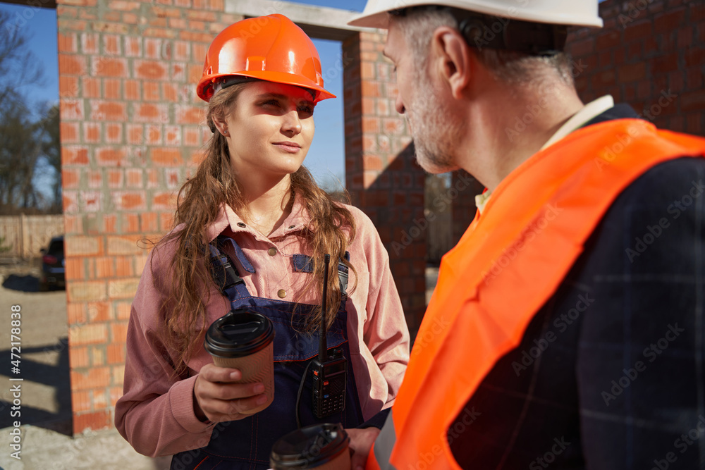 Ambitious woman in hardhat sharing coffee time with fellow worker Ambitious woman in hardhat sharing coffee time with fellow worker