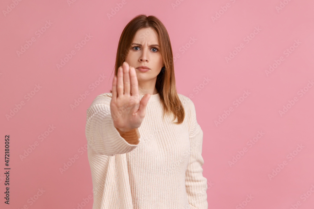 Portrait of serious strict young adult blond woman standing with stop hands gesture and caution to dont touch, wearing white sweater. Indoor studio shot isolated on pink background. Portrait of serious strict young adult blond woman standing with stop hands gesture and caution to dont touch, wearing white sweater. Indoor studio shot isolated on pink background.
