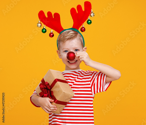 Cheerful little boy with wrapped Christmas gift holding red christmas tree ball in front of his nose
