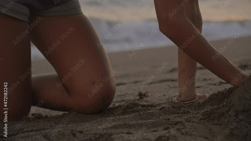 Tracking shot of Caucasian little boy and his mother building sand castle on beach at sunset Tracking shot of Caucasian little boy and his mother building sand castle on beach at sunset