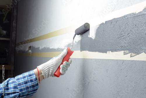 female painting a wall with masking tape and roller